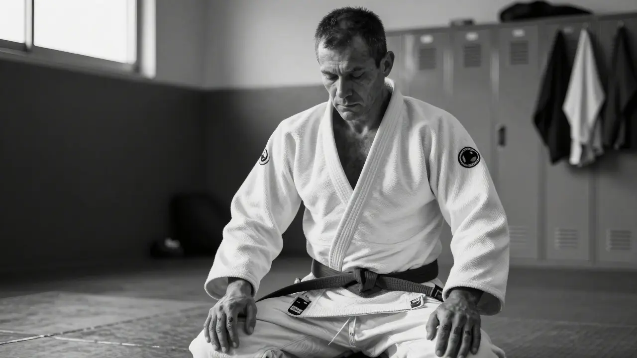 Judoka âgé assis seul après l'entraînement, mains sur les genoux, air de réflexion.